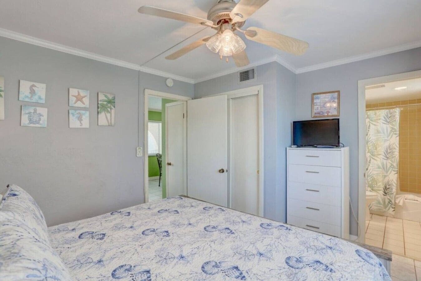 A bedroom with a bed, a ceiling fan, a dresser, and a television.