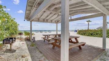 A beachside pavilion with picnic tables and a sandy walkway.