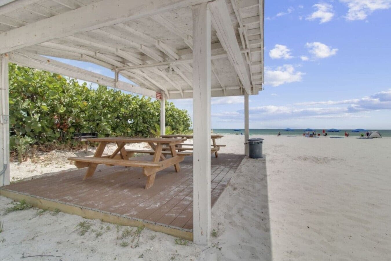 A beachside pavilion with picnic tables and a trash can.
