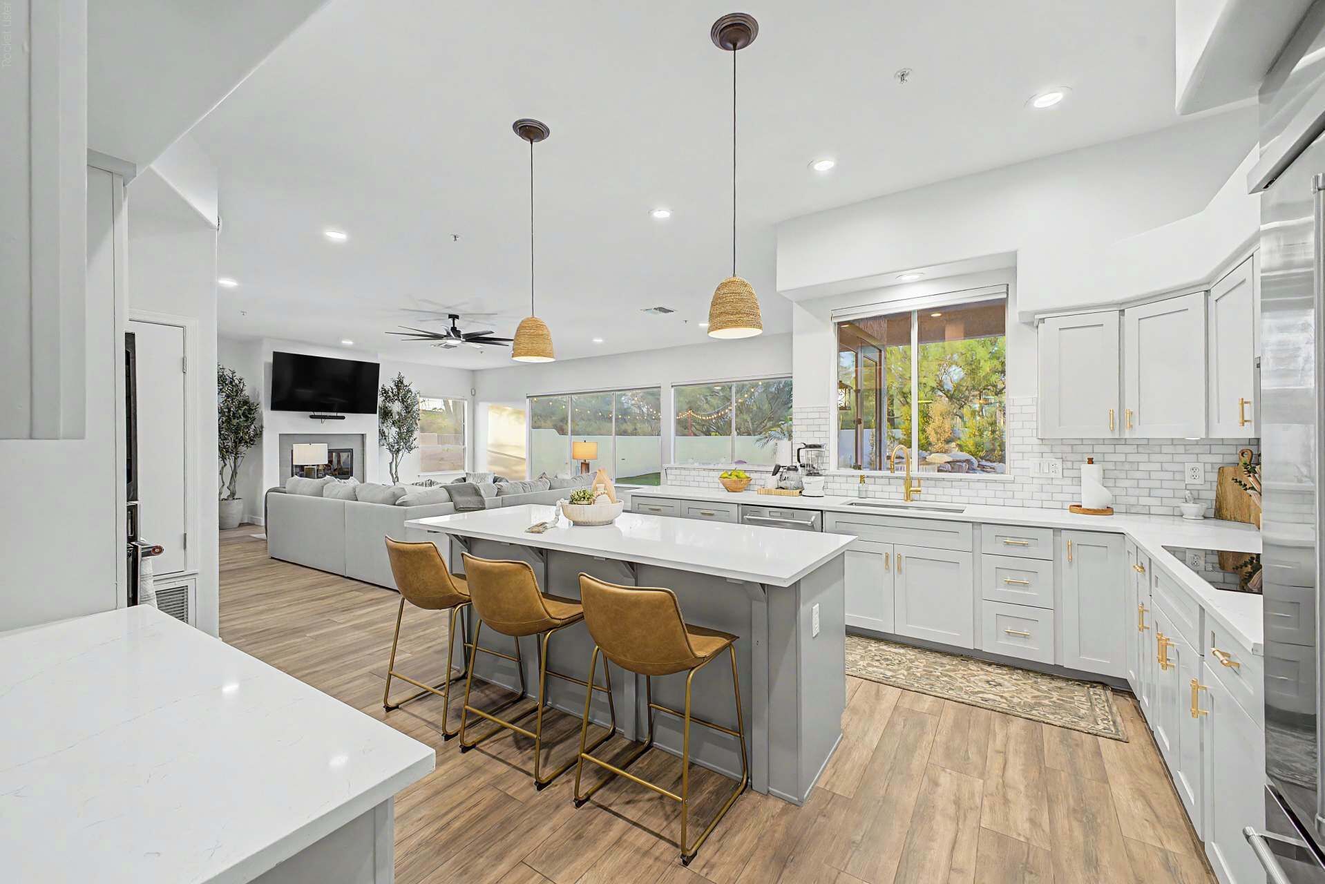 A modern kitchen with a large island, bar stools, and a dining area with a sofa.