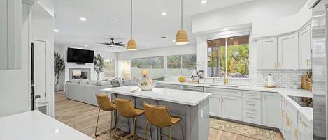 A modern kitchen with a large island, bar stools, and a dining area with a sofa.