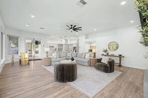 A modern living room with a sofa, ottoman, and coffee table, a dining area with chairs, and a kitchen in the background. - 4BR Scottsdale Getaway with Pool, Spa & Game Room (Scottsdale)
