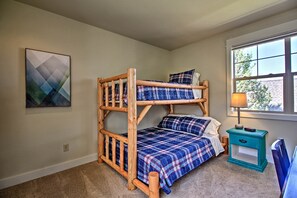 A bunk bed with a plaid bedspread, a small bedside table with a lamp, and a window with a view of trees.