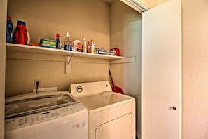 A laundry area with a washing machine, a dryer, and shelves above containing cleaning supplies.