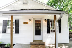 A white single-story house with black shutters, a front door, and a number '104' sign.