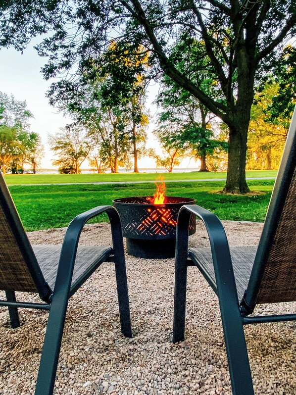 A fire pit with two chairs facing it, surrounded by gravel and trees.
