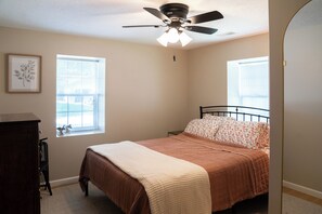 A bedroom with a bed, a ceiling fan, a dresser, and two windows.