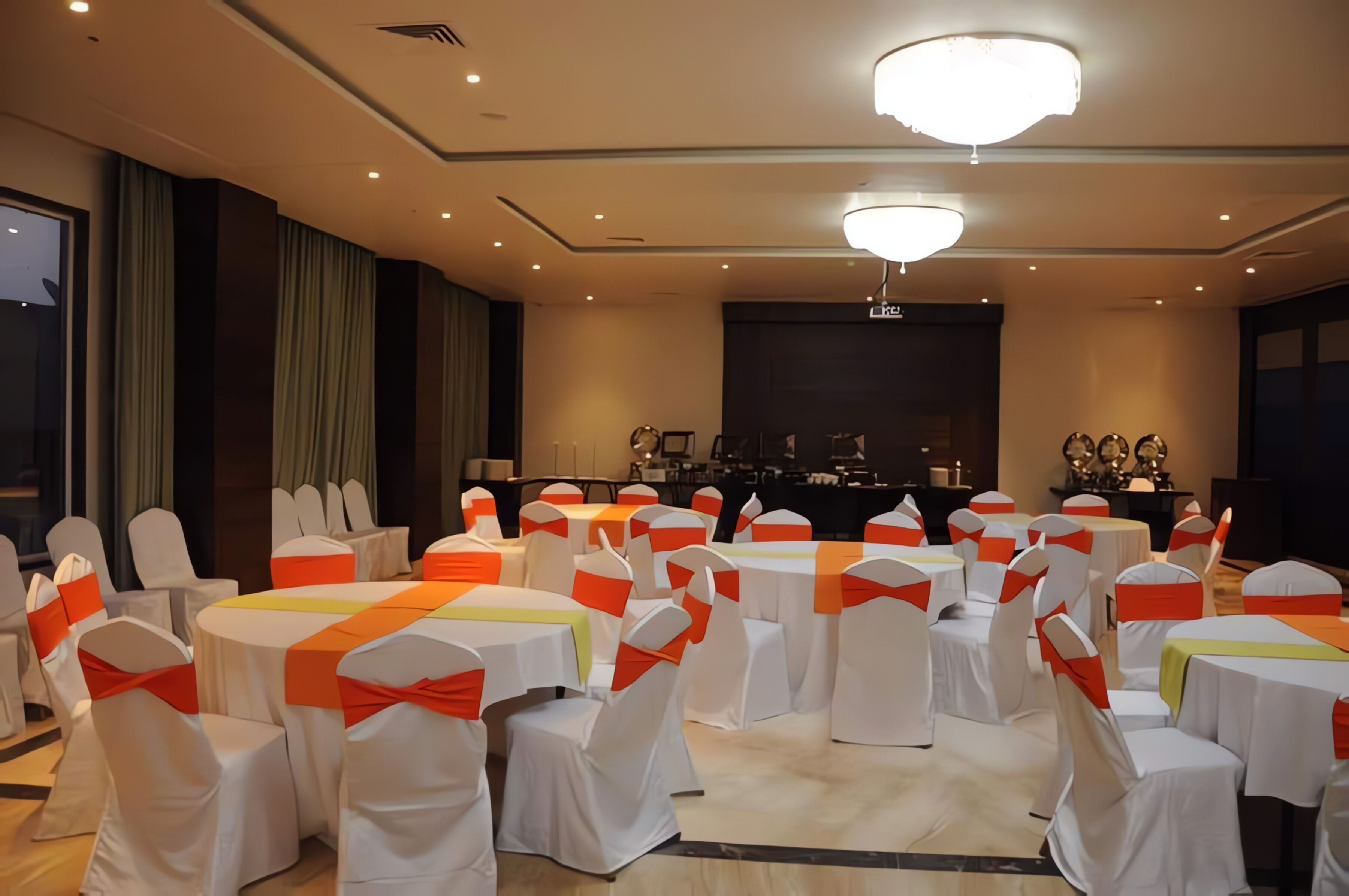 Un salón de conferencias con mesas y sillas redondas, un escenario con un atril y una gran lámpara de cristal.