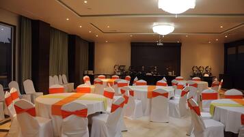Un salón de conferencias con mesas y sillas redondas, un escenario con un atril y una gran lámpara de cristal.