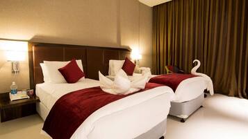 Habitación de hotel con dos camas, cada una con una colcha roja y almohadas blancas, un cabecero de madera y una mesita de noche con una lámpara y una botella.