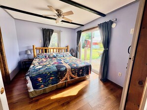 A bedroom with a wooden bed, a ceiling fan, a window with curtains, and a view of the outdoors.