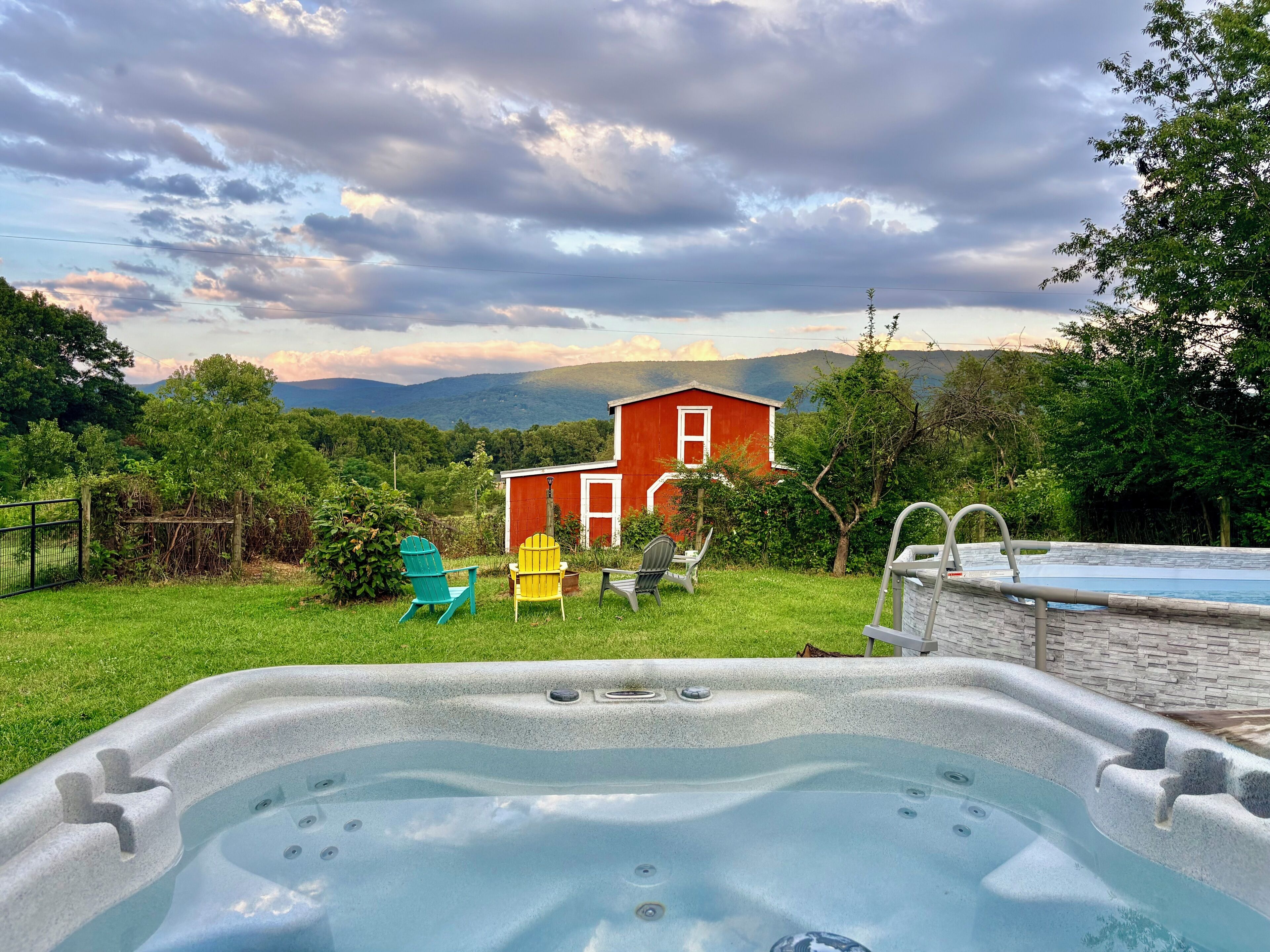 A hot tub with a view of a red barn and mountains in the background.