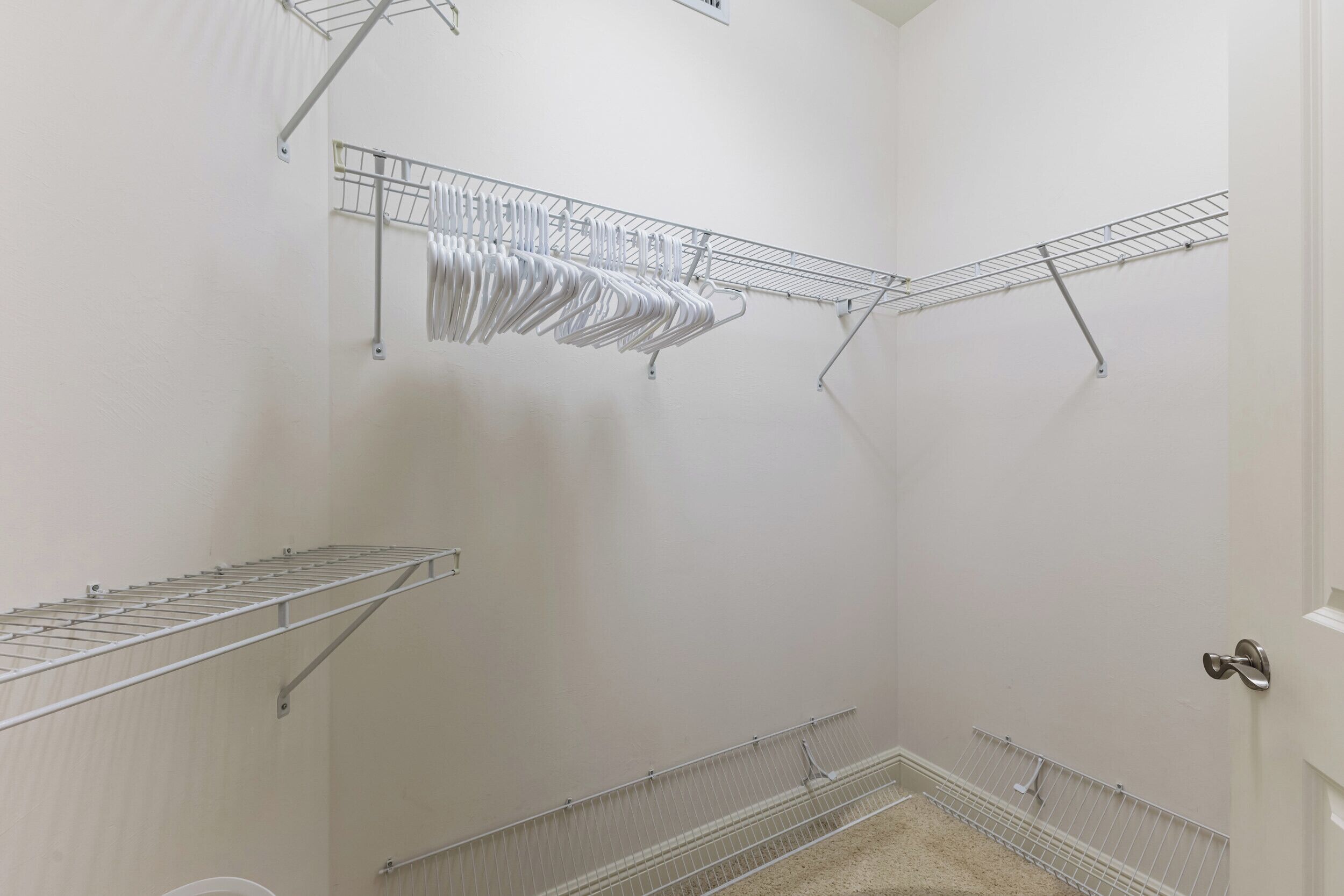 Una habitación con paredes blancas, una puerta con picaporte plateado y estanterías metálicas.