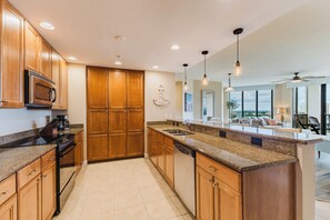 Une cuisine moderne avec des meubles en bois, un four à micro-ondes encastré, des plans de travail en granit et un grand îlot central doté d’un évier.