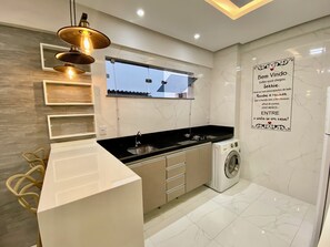 A modern kitchen with a built-in washing machine, a window, and a decorative wall sign. - 307 2Qtos Funcional bem Localizado (Belém)