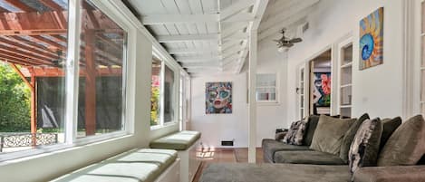 A spacious living area with a high ceiling, large windows, and a view of the outdoors.