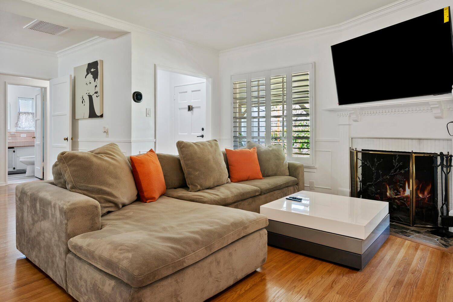 A living room with a beige sectional sofa, a white coffee table, a fireplace, and a mounted TV.