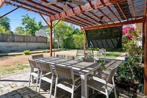 Eine überdachte Terrasse mit Tisch und Stühlen, einer Pergola und Kübelpflanzen.