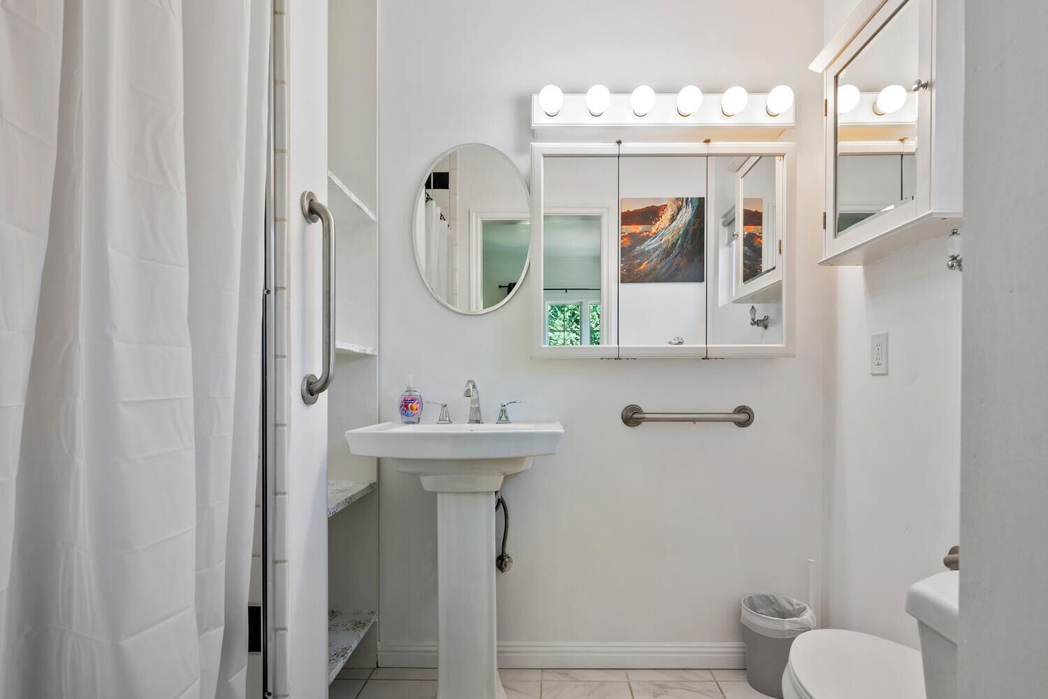 A bathroom with a white sink, a mirror with lights, and a shower curtain.