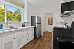 Eine moderne Küche mit weißen Schränken, einem Edelstahl-Kühlschrank, einem Gasherd und einem Fenster mit Blick auf Bäume.