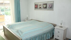 Een slaapkamer met een bed, nachtkastje, dressoir en een raam met gordijnen.