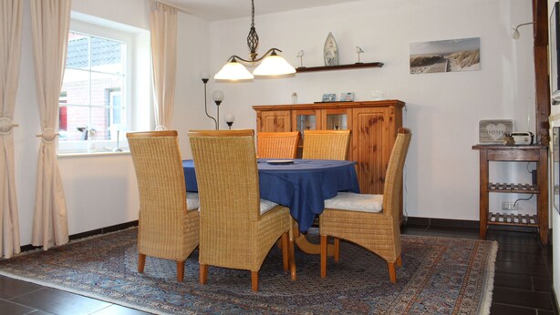 Een eetruimte met een tafel gedekt voor vier personen, omringd door rieten stoelen, een blauwe tafelkleed en een vloerkleed met dessin.