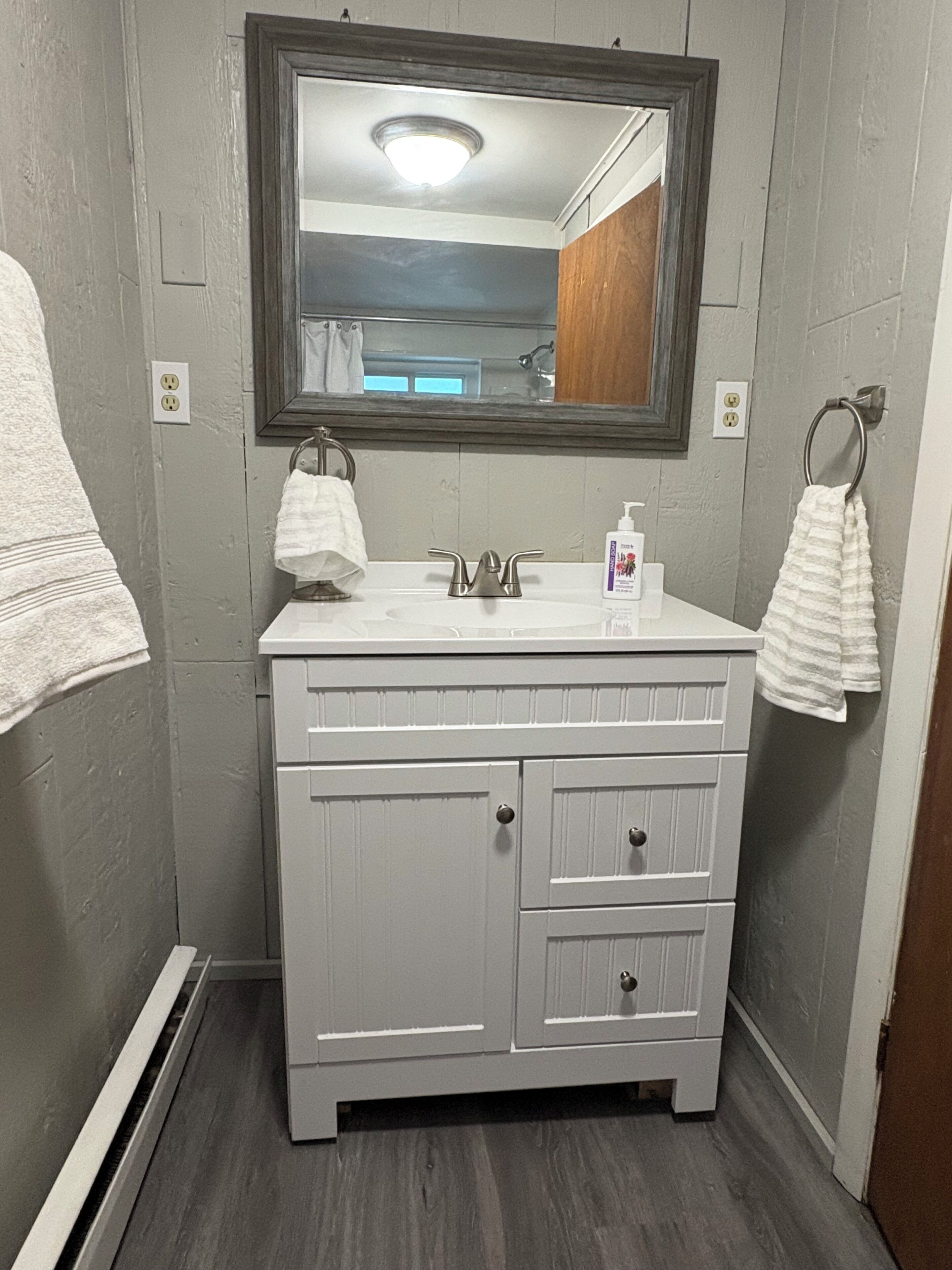 A bathroom with a white vanity, a mirror, a sink, and two towel rings.