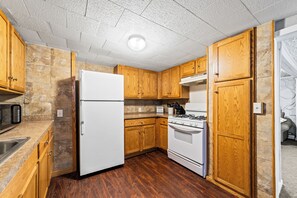 A compact kitchen with wooden cabinets, a white refrigerator, a stove, and a microwave. - Gorgeous 4-bedroom house with AC in quaint Fredonia (Fredonia)