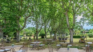 An outdoor seating area with tables and chairs, surrounded by trees. - L'HERMITAGE (Pernes-les-Fontaines)