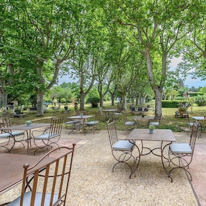 An outdoor seating area with tables and chairs, surrounded by trees.
