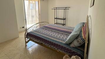 Ein Schlafzimmer mit Bett, einem Fenster mit Vorhängen, einem Heizkörper und einem Wandregal.