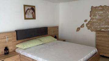 Een slaapkamer met een houten bedframe, een nachtkastje, een wandlamp en een lijst met een afbeelding aan de muur.