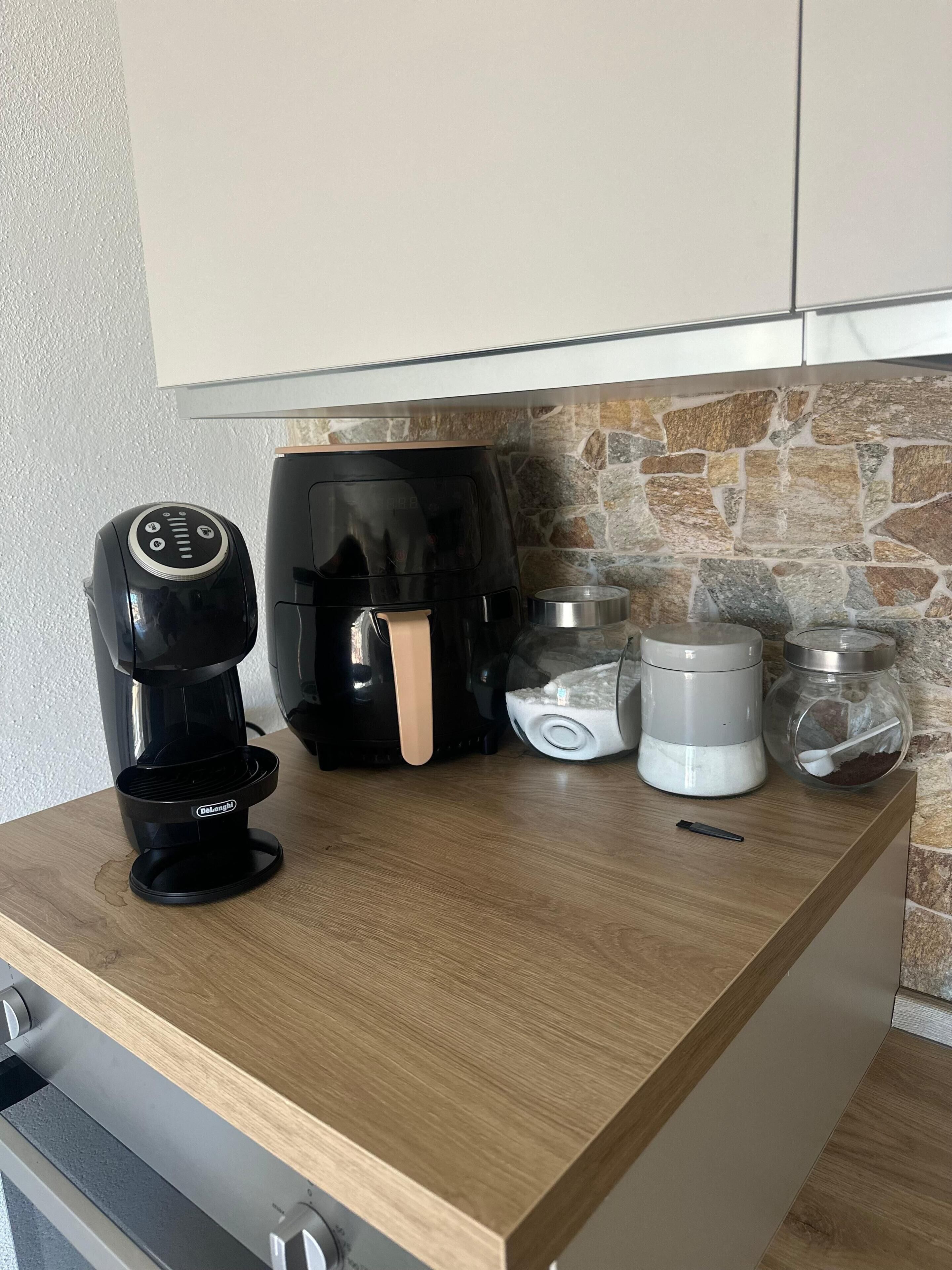 A kitchen counter with a coffee maker, a coffee machine, a water dispenser, and a jar with a spoon.