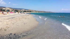 Una playa con aguas cristalinas, una orilla arenosa y colinas a lo lejos.