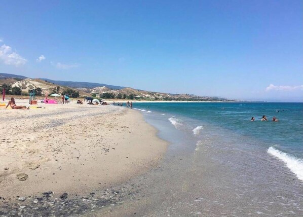 A beach with clear waters, a sandy shore, and distant hills.