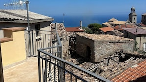 Un balcón con baranda metálica que da a un pueblo costero de arquitectura tradicional y un cielo azul despejado.