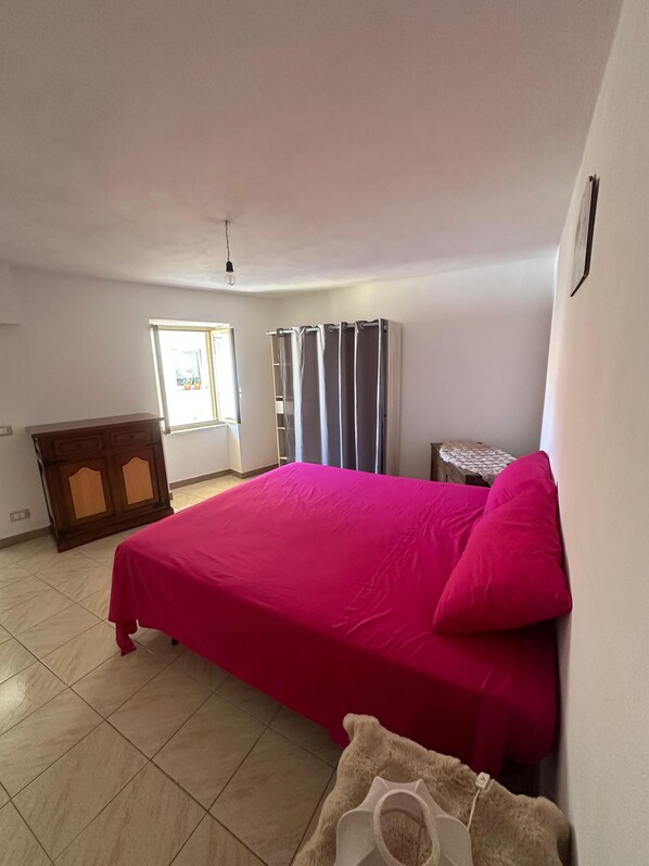 A bedroom with a bed, a dresser, a window, and a door.