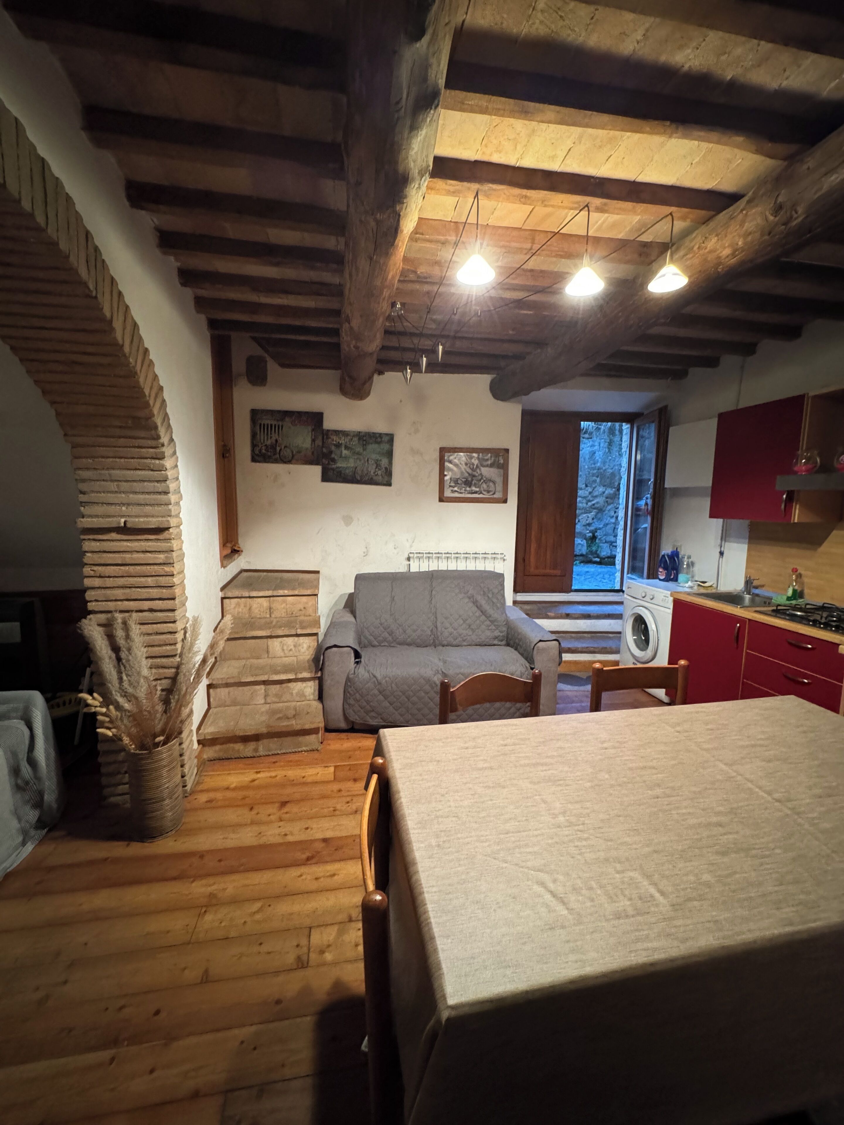 Een rustiek interieur met een houten trap, een bank, een eettafel en een keukenhoek.