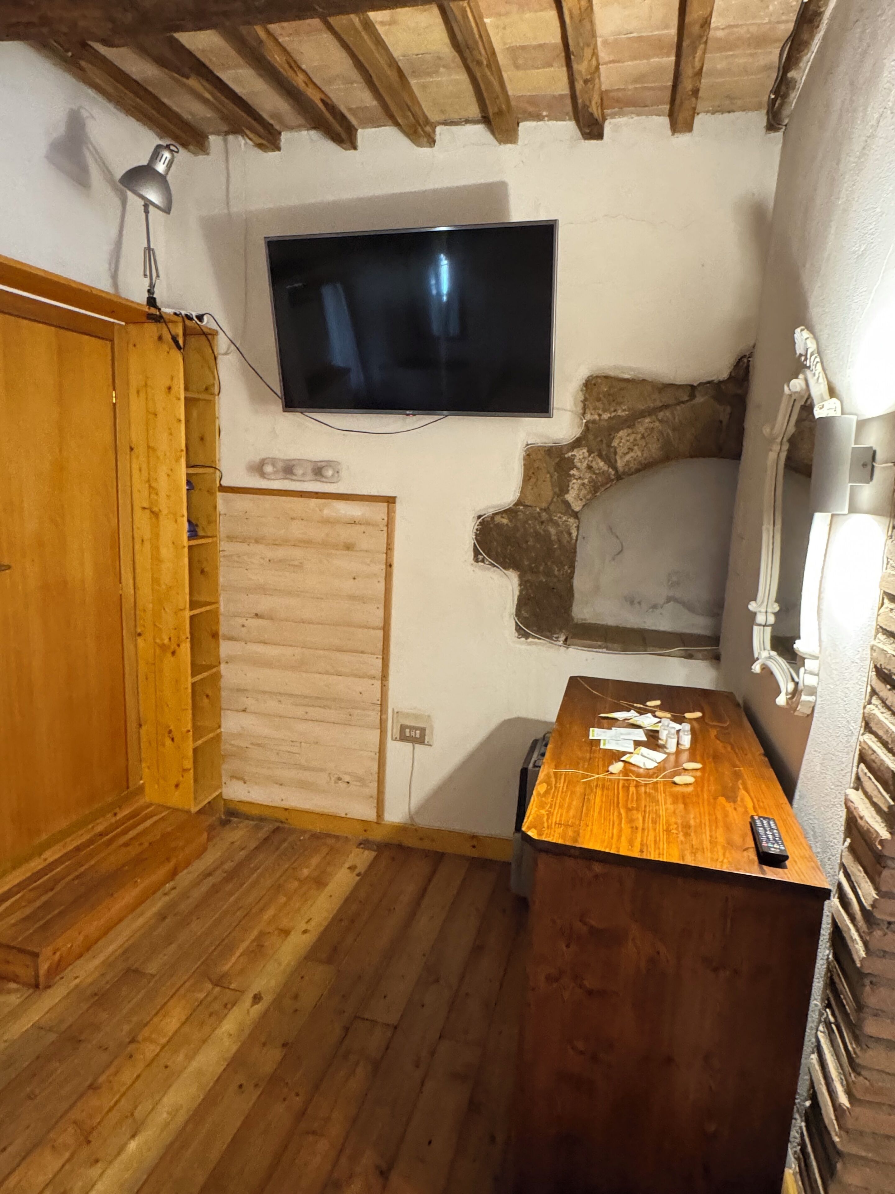 A room with a wooden floor, a television mounted on the wall, a wooden cabinet, and a small table with items on it.