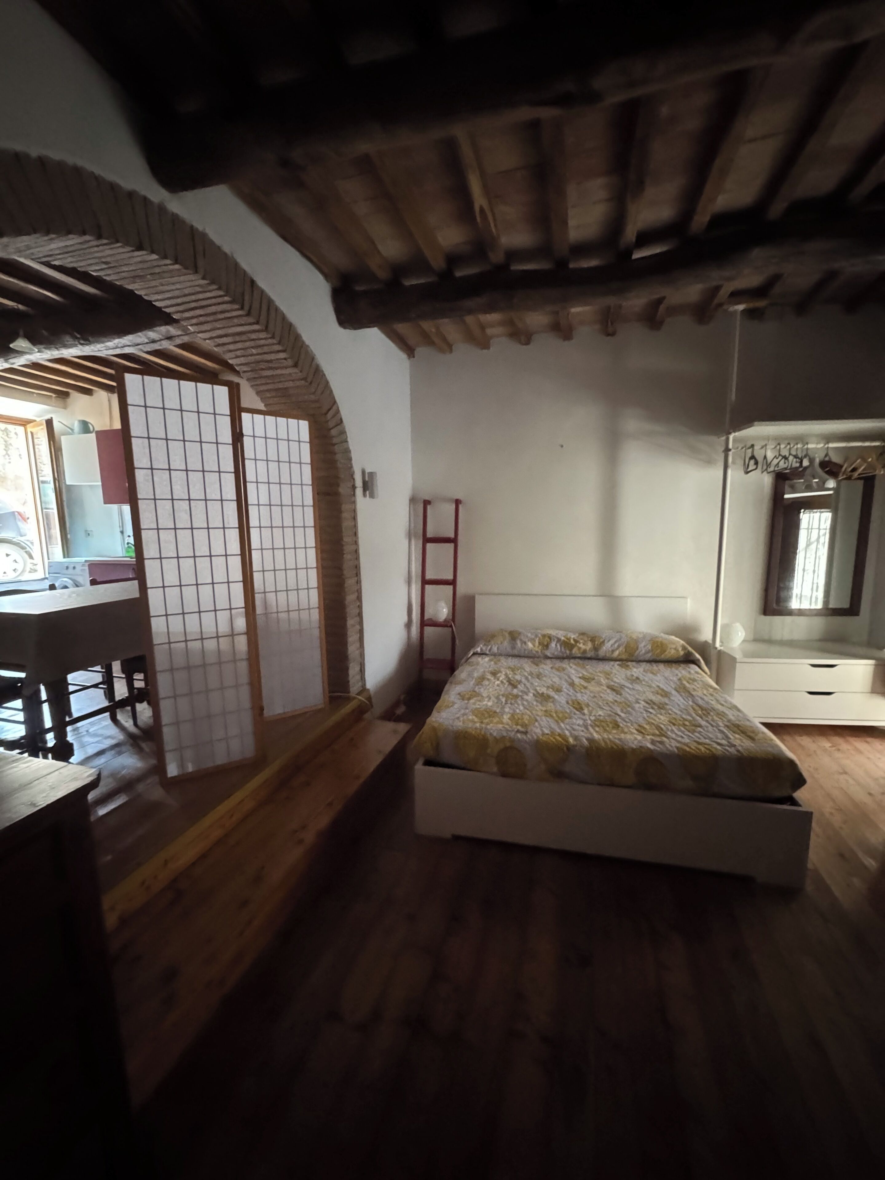 A bedroom with a wooden floor, a bed with a patterned bedspread, a red ladder, and a traditional Japanese shoji screen.