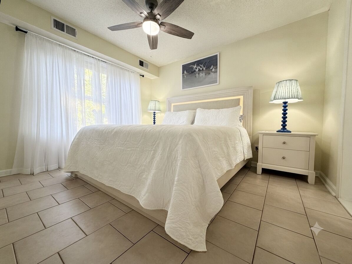 A bedroom with a bed, nightstands, a ceiling fan, and a window with curtains.