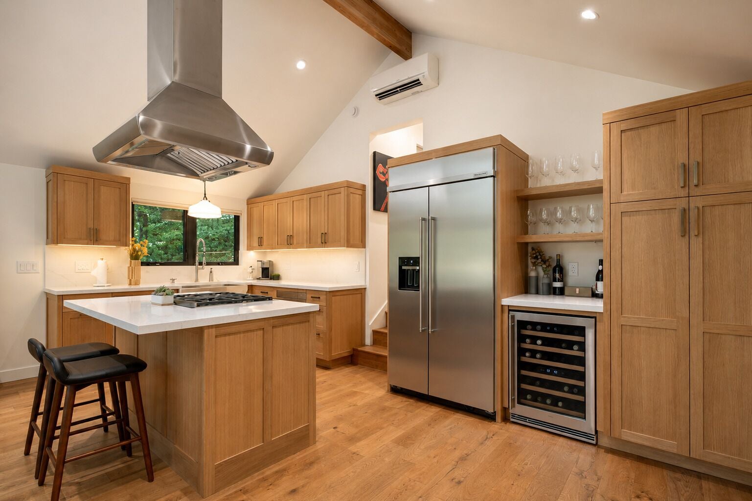 Une cuisine moderne avec des meubles en bois, un réfrigérateur en acier inoxydable, un réfrigérateur à vin et un grand îlot central doté d’une cuisinière à gaz.