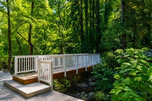 A wooden bridge with white railings over a stream, surrounded by lush greenery.