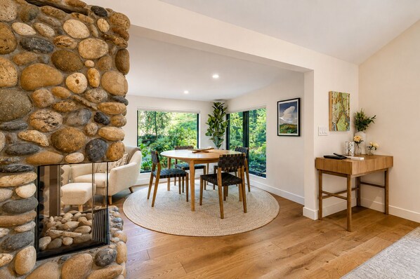 A dining area with a stone wall, wooden furniture, and a view of greenery.