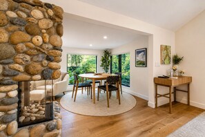 A dining area with a stone wall, wooden furniture, and a view of greenery.