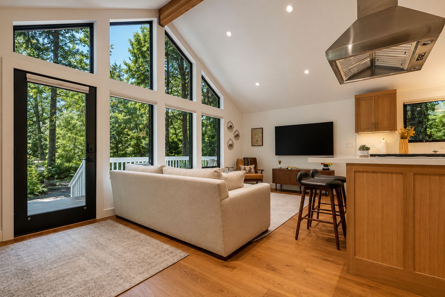 A modern living room with a sofa, a TV, and a kitchen area with wooden cabinets and a large window.