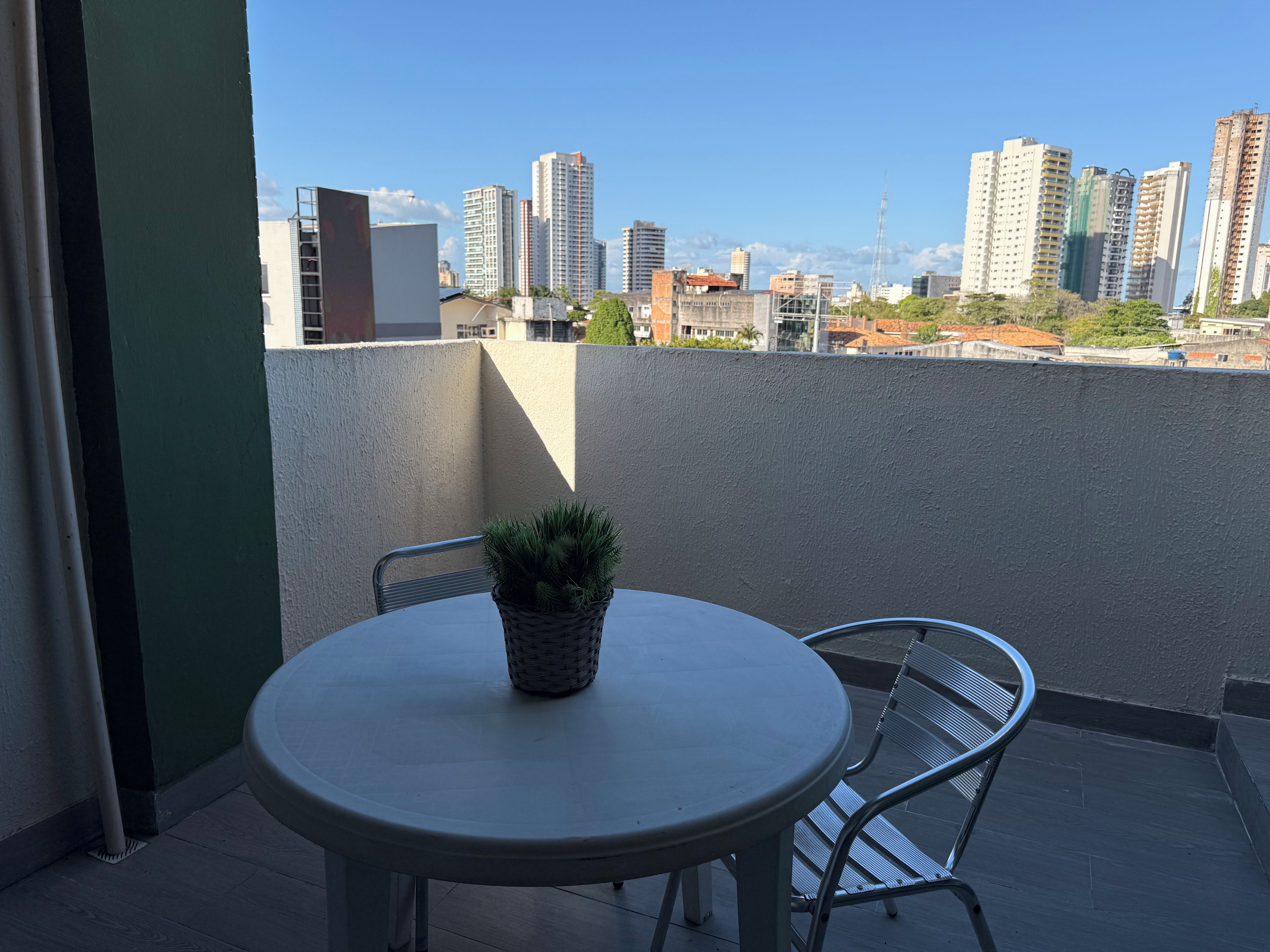 Un balcón con una mesa redonda y sillas, una planta en maceta y vista a la ciudad.