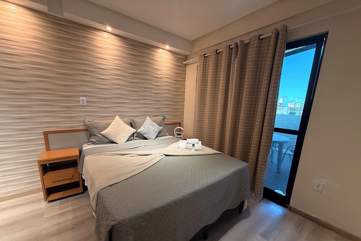A modern bedroom with a large bed, a wooden nightstand, and a view of the city through a window.