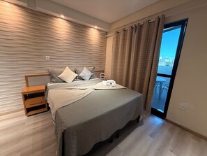 A modern bedroom with a large bed, a wooden nightstand, and a view of the city through a window. - 401 Suite Elegante e Moderna (Belém)
