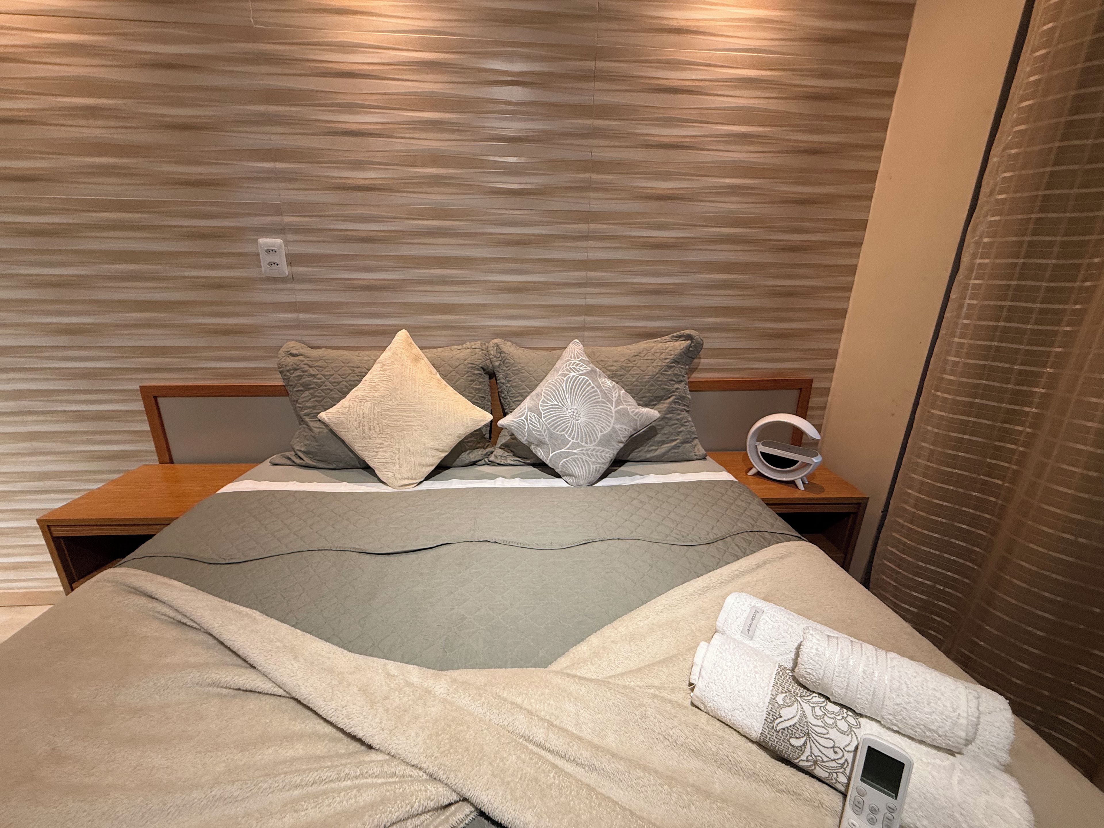 A neatly made bed with a quilted headboard, two pillows, and a remote control on a bedside table.